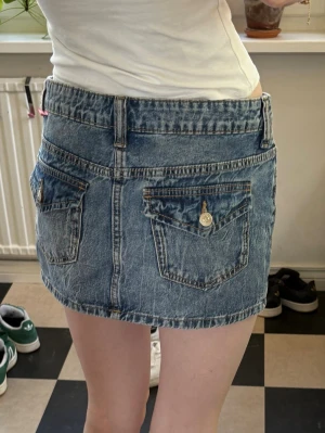 Blå jeanskjol med fickor - Säljer en blå jeanskjol i klassisk denim med två stora bakfickor och bälteshällor. Kjolen har en kort passform och stängs med knapp och dragkedja framtill. Perfekt för dig som gillar en enkel men snygg look. 💕💕