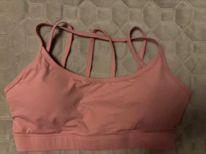 Rosa sport-bh med flera axelband - Säljer en snygg rosa sport-bh med flera tunna axelband i ryggen för en trendig look. Bh:n är tillverkad i ett stretchigt och mjukt material som ger bra stöd och komfort. Perfekt för dig som gillar en sportig och modern stil.