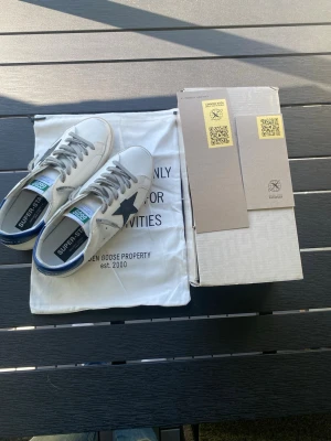 Golden Goose - Golden Goose Superstar sneakers i vitt läder med gråa snören och en svart stjärna på sidan. Aldorg använda 10/10 skick. Snabb affär 🏬 snabb leverans 📦 på samma dag. Skriv vid funderingar. Storlek 44 men passar samt 45.