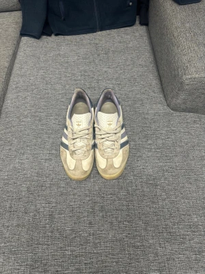 Adidas sneakers med blå ränder - Säljer ett par klassiska Adidas sneakers med beige mocka och blå ränder på sidorna. Skorna har låg profil och gummisula, samt snörning framtill. Perfekta för dig som gillar retrostil och ikoniska detaljer nypris 2600