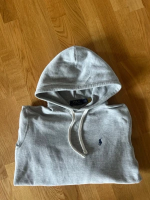 Grå hoodie från Polo Ralph Lauren XS - Snygg grå hoodie från Polo Ralph Lauren med klassisk huva och dragsko. Tröjan har det ikoniska lilla blå logobroderiet på bröstet och är tillverkad i mjuk bomullsblandning. Perfekt för en avslappnad och stilren look. Storlek xs sitter xs fast nästan lite litet. Skulle passa om man är runt 165-175 typ beroende på hur den ska sitta
