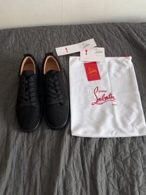 Christian Louboutin skor  - Stilrena svarta sneakers från Christian Louboutin i mocka med matchande svarta skosnören och sula. Klassisk låg modell med diskret logga och snygga detaljer. Kommer med originalpåse och tags.