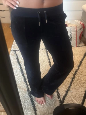 Mörkblå mjukisbyxor från juicy couture  - Säljer ett par mörkblå mjukisbyxor i mjuk velour med raka ben och dragsko i midjan. Byxorna har fickor fram och dekorativa knappar på bakfickorna. Perfekta för chill dagar hemma eller när du vill vara extra bekväm.