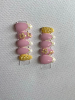 Press-on naglar rosa och gula blommor - Söta press-on naglar i mandelform med rosa bas, vita prickiga tippar och detaljer i gult. Några naglar har 3D-blommor och andra har swirl-mönster i gult. Perfekt för dig som vill ha en färgglad och unik nageldesign.