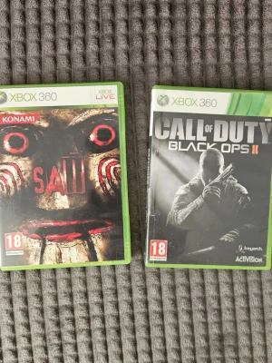 Xbox 360 spel: Saw & Black Ops II - Två Xbox 360-spel: Saw från Konami med skräcktema och Call of Duty: Black Ops II från Activision, ett actionfyllt FPS. Båda spelen har gröna plastfodral och tydliga omslag. Perfekt för dig som gillar skräck eller intensiva shooters.