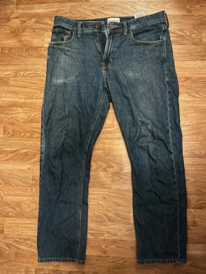 Jeans  - Säljer ett par mörkblå jeans från Stock n Hank med rak passform och klassisk femficksdesign. Jeansen har normal midja och är tillverkade i kraftig denim med kontrastsömmar. Perfekta för en avslappnad och stilren look.