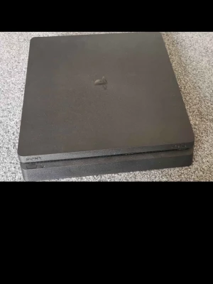PlayStation 4 Slim med två kontroller - Säljer en svart PlayStation 4 Slim från Sony tillsammans med två matchande svarta DualShock 4-kontroller. Konsolen har en stilren, fyrkantig design i matt plast och är perfekt för gamingkvällar med vänner.