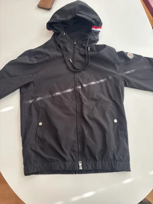 Svart vindjacka från Moncler - Snygg svart vindjacka från Moncler med huva och dragkedja framtill. Jackan har använts ungefär 5-7ånger, tveka inte på att höra av er ifall det är frågor! Scan fungerar inte