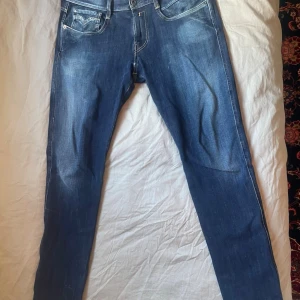 Blå slim fit jeans från Replay - Säljer ett par blå slim fit jeans från Replay med snygga slitningar och kontrastsömmar. Jeansen har klassisk femficksmodell, normal midja och smal passform. Materialet är mjukt denim med stretch för extra komfort. Perfekta för en trendig och avslappnad look. MODELLEN ÄR 181 CM LÅNG.