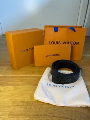 Svart läder skärp - Snyggt svart skärp från med klassiskt monogrammönster och L -spänne. Skärpet är gjort i skinn och har en stilren look som passar till många outfits. Levereras med originalpåse och box.