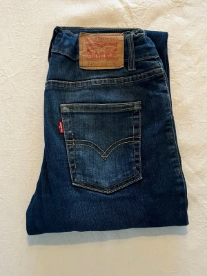 Levi's 512 blå jeans Slim Taper - Snygga blå, klassiska Levi's 512 jeans. Jeansen har en mörk tvätt, kontrastsömmar och ikonisk läderpatch bak i midjan. Perfekta för en avslappnad och tidlös look. Barnstorlek. Lite slitage på bakre läderpatch.
