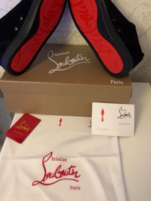 Svarta sneakers från Christian Louboutin - Snygga svarta sneakers från Christian Louboutin med ikoniska röda sulor och diskret logga på sidan. Skorna har en låg profil, svarta skosnören och är tillverkade i mocka. Perfekta för dig som vill sticka ut med exklusiv design och streetkänsla. HELT OANVÄNDA SKOR!!!  Våga skriva gärna pris kan diskuteras 