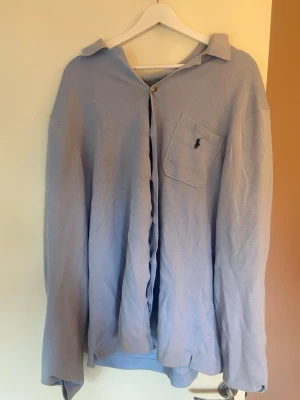 Ljusblå skjorta från Ralph Lauren - Klassisk ljusblå skjorta från Ralph Lauren med bröstficka och broderad logga. Skjortan har knappar framtill och lång ärm. Perfekt för en clean och stilren look.
