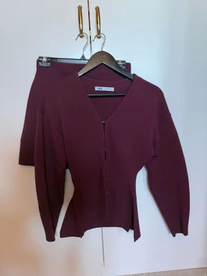 Vinrött set från Zara med kjol och topp - Säljer ett vinrött set från Zara med långärmad topp och matchande kjol. Toppen har v-ringning, knappar framtill och en cool slitsdetalj i sidan. Kjolen är kort och figurnära. Materialet är stretchigt och mjukt, perfekt för en trendig look. OBS! Kjolen är i S men tröjan i XS