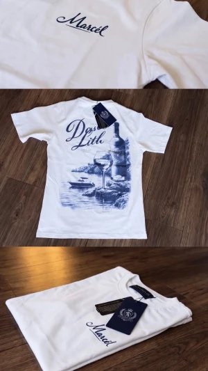 Vit t-shirt från Marcel med tryck - Vit t-shirt från Marcel med blått tryck på ryggen som föreställer vinflaska, glas och havsmotiv. Framsidan har diskret Marcel-logga i blått. Klassisk rund hals och korta ärmar. Perfekt för dig som gillar stilrena motiv och snygga detaljer.