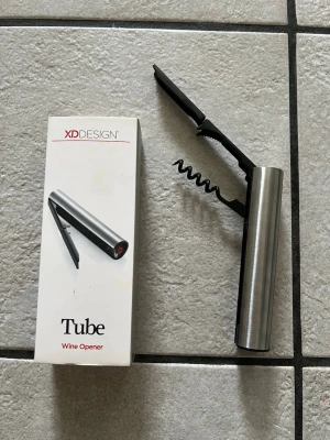 Vinöppnare Tube från XD Design - Säljer en stilren vinöppnare Tube från XD Design i metall och svart plast. Den har en cylinderformad kropp i borstat stål och klassisk korkskruv samt folieskärare. Perfekt till hemmabaren eller som present till vinälskaren.