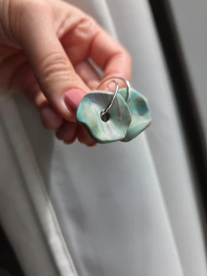 Gröna swirlade örhängen i polymerlera - Unika örhängen med oregelbunden form i grönt, grått, blått och lite guld med swirl-effekt. Tillverkade i polymerlera och har silvriga ringar i metall. Örhängena är tillverkade för hand av mig i polymerlera och är one of a kind.