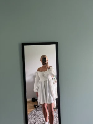 Vit offshoulder kort klänning - Söt vit kort klänning med offshoulder och långa puffärmar. Klänningen har smock över bysten och midjan vilket ger en fin passform. Perfekt för sommardagar och har en luftig, flowy känsla.