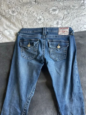 True religion joey Lågmidjade  - Märke: True religion  Storlek: 25 motsvarar XS  Färg: Mörkblå med gula sömmar på bakfickorna  Modell: Joey low Rise  Utseende: Klassisk femficks design, Lågmidjade jeans med utsvängda ben. Sitter super snyggt och har gula sömmar   Dem är väldigt fina och är i super skick (se bilder) dem har använts fåtalet gånger därav säljs dem. I princip nya. Passar perfekt till sommar och höst. 🌸 Ge förslag!