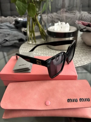 Svarta solglasögon från Miu Miu - Stilrena svarta solglasögon från Miu Miu med fyrkantig form och breda bågar. Loggan syns i guld på sidan. Kommer med rosa fodral och originalförpackning. Perfekta för dig som vill ha en trendig accessoar med lyxig känsla. Dom är är väldigt bra skick och knappt använda, fick de i present men tycker ej de passar mig därav säljer jag dom🤗🙌🏼💕