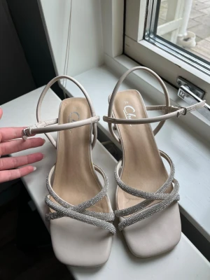 Beige pumps med silverglitter - Säljer ett par snygga beige pumps med fyrkantig tå och tunna remmar dekorerade med glittrande strass. 