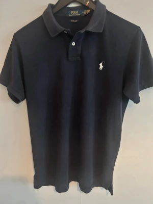Polo Ralph Lauren piké - • 🇸🇪 Marin blå Piké från Polo Ralph Lauren. Broderad logga på bröstet.   Använd, men fortfarande i fräscht skick utan några speciella anmärkningar. Den är dock lite mindre i storlek, så om du har S passar denna dig!  Pris går alltid att diskutera vid snabb affär 🥂 