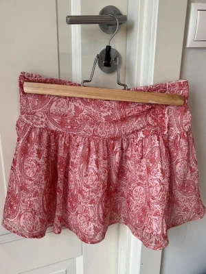 Gina Tricot rosa mönstrad sommarkjol - Jag säljer en söt, rosa och kort sommarkjol med vitt paisleymönster från Gina Tricot i storlek 146/152. Kjolen är knappt använd och därför i nyskick. 