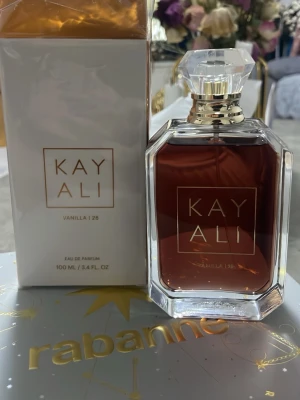 Kayali Vanilla | 28 Eau de Parfum - Kayali Vanilla | 28 Eau de Parfum är en lyxig parfym med varm vaniljdoft. Flaskan är elegant och genomskinlig med guldiga detaljer och en kristalliknande kork. Förpackningen är vit med guldtext och rymmer 100 ml. Perfekt för dig som älskar söta och sofistikerade dofter.