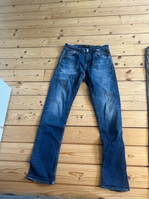 Blå raka jeans från Replay - Säljer ett par klassiska blå jeans från Replay Jeans med rak passform och snygga slitningar framtill. Jeansen har fem fickor, knappgylf och kontrastsömmar. Perfekta till en avslappnad stil och tillverkade i bomull.