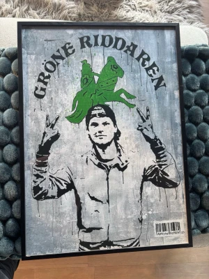 Tavla Gröne Riddaren  - Unik tavla med street art-motiv av en person som gör peace-tecken och en grön riddare på häst ovanför. Texten 'GRÖNE RIDDAREN' upptill och signatur med streckkod nertill. Grå bakgrund och svart ram. Ensast poster medföljer!