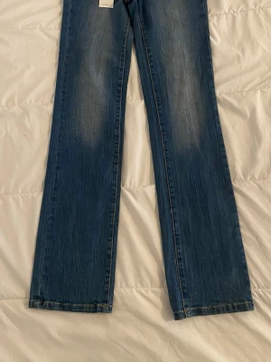 Blå raka jeans från Vero Moda - Snygga blå jeans från Vero Moda med regular fit och normal midja. Jeansen har raka ben och klassisk femficksdesign. Tillverkade i denim med lätt slitna detaljer framtill för en avslappnad look.