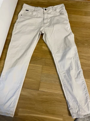Beige chinos från Lee - Snygga beige chinos från Lee med klassisk femficksdesign och smal passform. Tillverkade i mjukt bomullstyg som ger en skön känsla och stilren look. Perfekta för dig som gillar en clean och enkel stil.