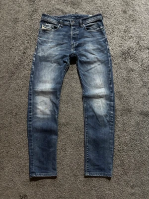 Diesel jeans - Säljer ett par blå slim fit jeans från Diesel med snygga slitningar och tvättade detaljer på låren och knäna. Klassisk femficksmodell med logotyp på myntfickan. Perfekta för en avslappnad och trendig look.