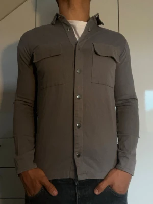 Grå overshirt från Galiente - Grå overshirt från Galiente tillverkad i 100% bomull. Strl S. Inga defekter. Modellen är 178 cm och väger 77 kg. Hör gärna av dig vid frågor!