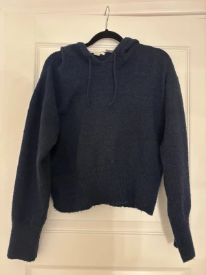 Mörkblå stickad hoodie - Mysig mörkblå stickad hoodie med huva och dragsko. Tröjan har långa ärmar. Super skön!