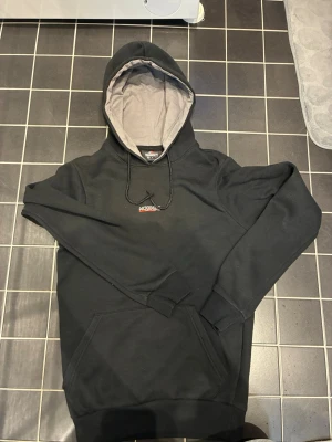 Svart hoodie från MCKENZIE - Säljer en svart hoodie från Napapijri med grå insida i huvan och klassisk logga på bröstet. Hoodien har känguruficka framtill, ribbade muddar och dragsko i huvan. Perfekt för dig som gillar streetwear och vill ha en enkel men snygg look.