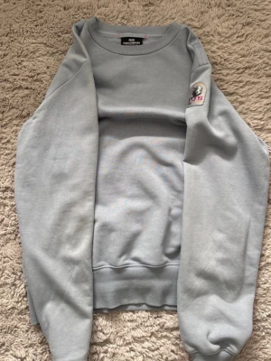 Ljusblå sweatshirt från Parajumpers - Snygg ljusblå sweatshirt från Parajumpers med rund halsringning och ribbade muddar. Tröjan har en patch med logga på ena ärmen och är tillverkad i mjukt bomullsmaterial. Perfekt för en avslappnad och stilren look.
