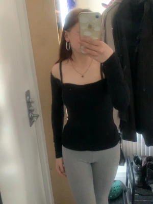 Svart offshoulder topp med lång ärm - Trendig svart offshoulder topp med långa ärmar och smala axelband. Sitter tight och har en stilren, enkel design som passar perfekt till jeans eller kjol. Materialet känns mjukt och följsamt mot kroppen.