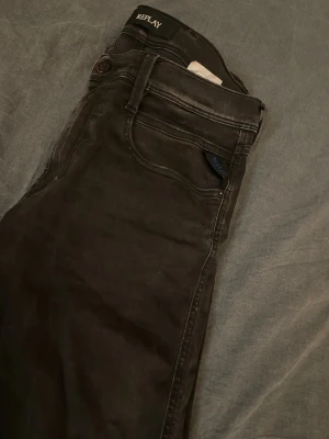 Svarta jeans från Replay - Säljer ett par svarta jeans från Replay med klassisk femficksdesign och snygga detaljer på bakfickan. Jeansen är i storleken 31/32. Jeansen har en slim fit och är tillverkade i stretchigt denim som ger en skön passform. Perfekta för dig som gillar stilrena och moderna jeans.