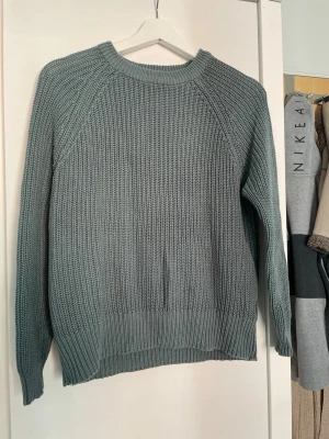 Grönblå stickad tröja i grovstickat - Snygg grönblå stickad tröja i grovstickat material med rund halsringning och långa ärmar. Tröjan har ribbade muddar vid ärmslut och nederkant, perfekt för lager-på-lager-stil. Enkel och stilren design som passar till det mesta.