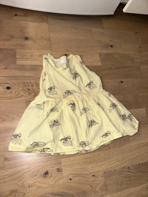 Gul klänning med insektsmönster - Gul klänning med insektsmönster Söt gul klänning från KappAhl med svartvitt insektsmönster. Ärmlös modell med rund halsringning och utställd kjol. Tillverkad i mjukt bomullstyg, perfekt för en avslappnad och trendig look.