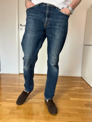 Levi's blå raka jeans herr - Klassiska blå jeans från Levi's med rak passform och normal midja. Jeansen har fem fickor, subtila slitningar och kontrastsömmar. Tillverkade i slitstark denim med den ikoniska röda Levi's-lappen på bakfickan.