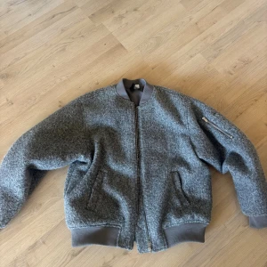 Grå oversize bomberjacka i ullmix st XS - Snygg grå bomberjacka i ullmix med ribbade muddar och krage. Jackan har dragkedja framtill, två fickor på sidorna och en ärmficka med dragkedja. Använd max 3 gånger