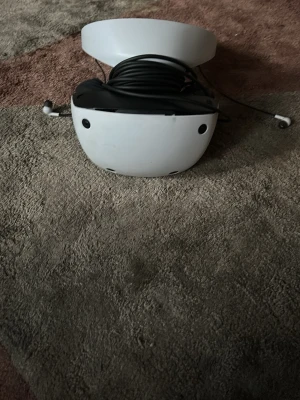 PlayStation VR2 headset med kabel - Säljer ett PlayStation VR2 headset från Sony. Glasögonen är vita med svarta detaljer och har en rundad, futuristisk design. Medföljande kabel är virad runt headsetet. Materialet är plast med mjuka insidor för bekväm passform. Perfekt för dig som vill ta gaming till nästa nivå.. 