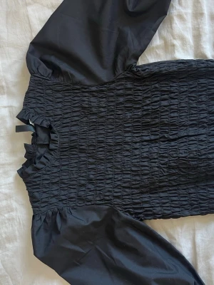 Svart blus - Säljer denna supersöta svarta blusen från HM då den tyvärr är förliten för mig. Ärmarna trekvart och lite lätt puffiga. Baksidan är helt plain och framsidan lite rynkad. Har tyvärr inga bilder på då den är alldeles för liten för mig🙈💕
