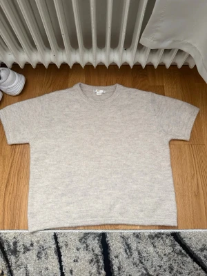 Beige stickad t-shirt  - Säljer en beige stickad t-shirt från Gina Tricot med rund halsringning och korta ärmar. Passar XS. Tröjan har en enkel och stilren design med ribbstickad kant vid halsen. Perfekt för dig som gillar en avslappnad och trendig look.