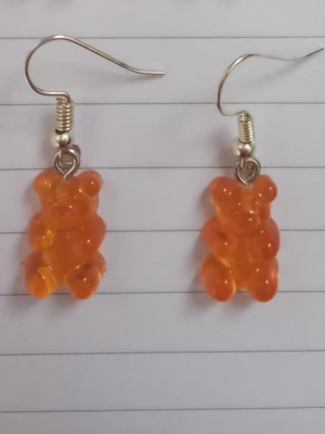 Orange björn örhängen - Säljer ett par unika örhängen med orange gummibjörns-hängen i plast. Örhängena har krokar i metall och är knappt använda. 