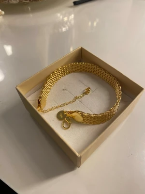   18K Guldpläterad armband  - Snyggt och brett armband i 18K guld med en elegant kedjedesign. Armbandet har justerbar längd och en rund bricka vid låset som markerar 18K. Perfekt accessoar för att lyfta din stil med en lyxig touch.