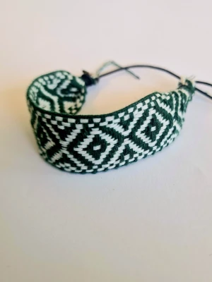 Grönvit vänskapsarmband med mönster - Snyggt handgjort vänskapsarmband i grönt och vitt med geometriskt mönster. Armbandet är gjort av flätad tråd och har justerbar knytning för perfekt passform. Perfekt accessoar för att ge din stil en personlig touch.