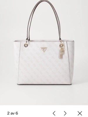 Vit shoppingväska från Guess - Snygg stor vit shoppingväska från Guess med diskret logomönster över hela väskan. Väskan har två långa handtag och en dekorativ tag med Guess-logga. Perfekt för dig som vill ha mycket plats för allt och ändå se trendig ut. Väskan ser större ut än på bild, skickar gärna egna bilder i fall man är intresserad! Använd kanske 3 ggr för länge sedan, sedan bara stått. 